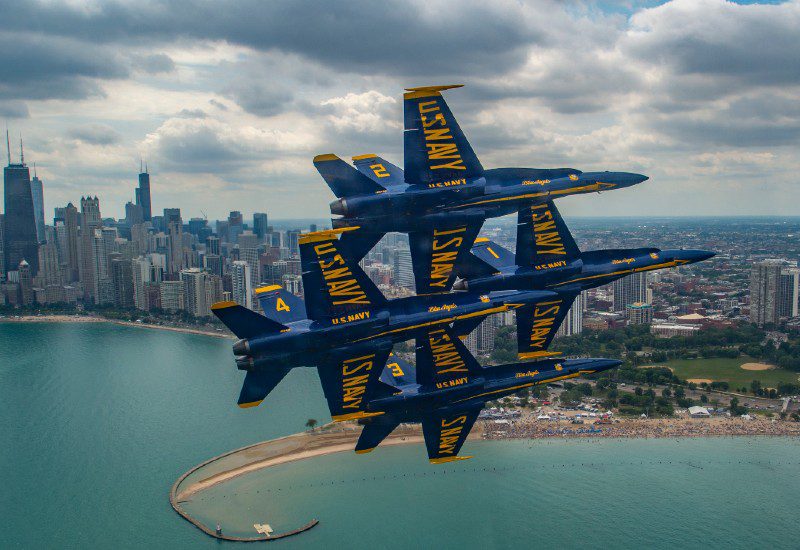 Blue Angels flying over city bay in diamond formation.